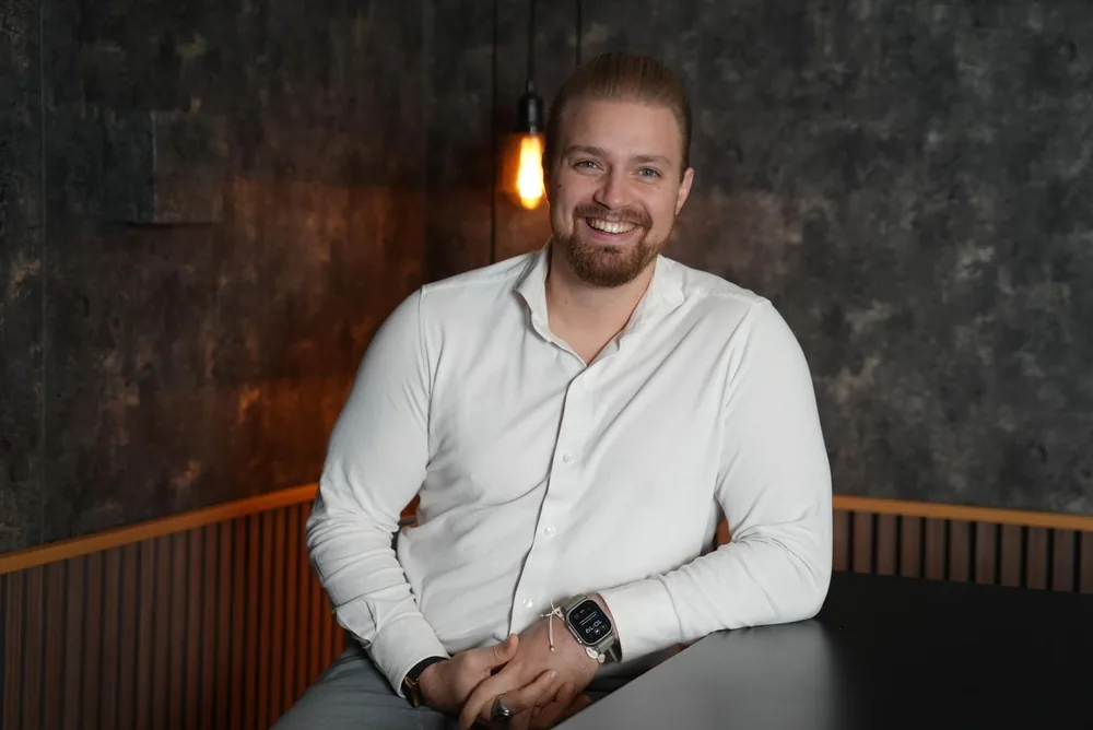 Francesco Jäger lächelt im weißen Hemd, an einen Tisch gelehnt